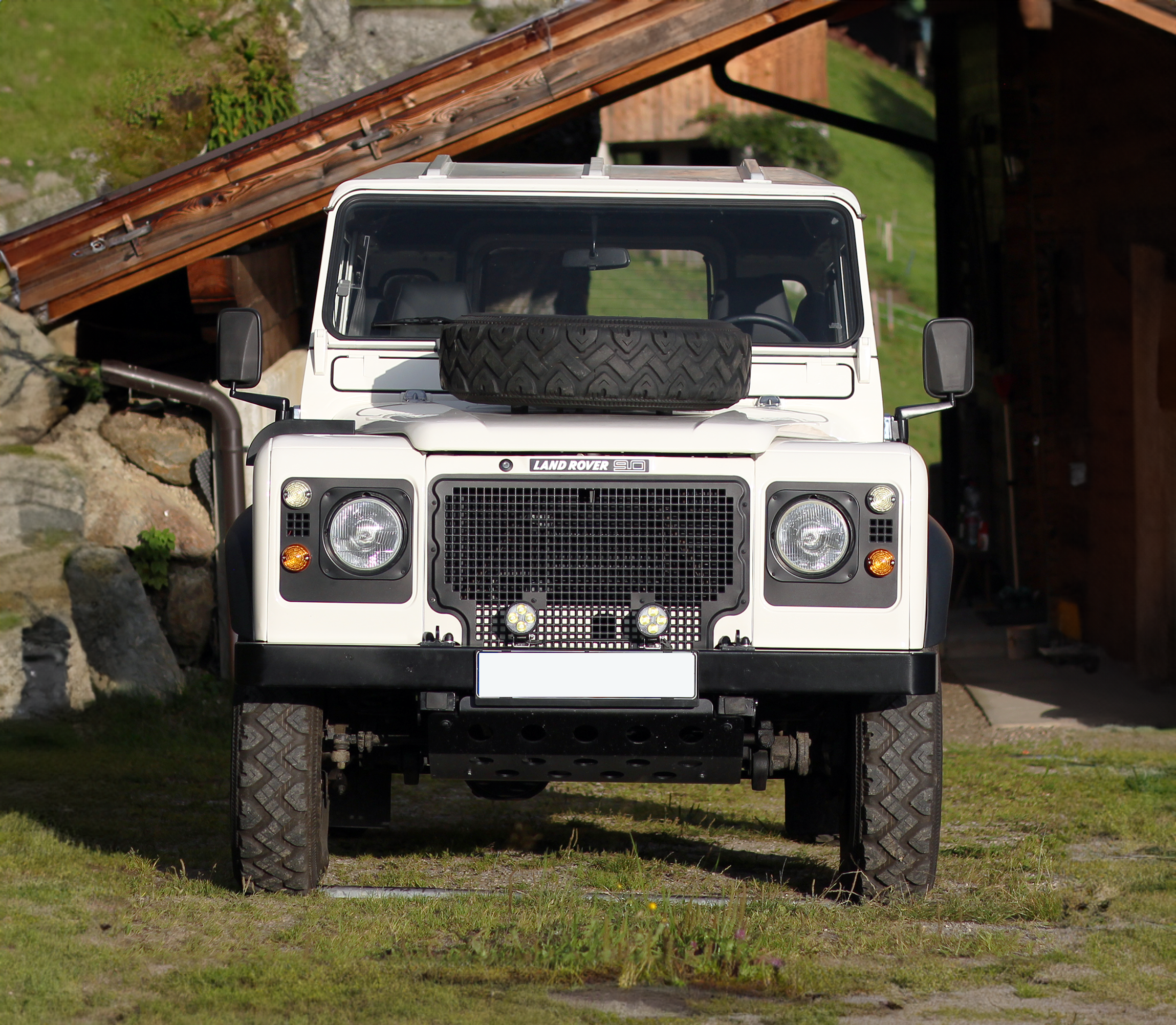 weißer restaurierter Land Rover Defender 90 frontal vor einer Berghütte in den Alpen