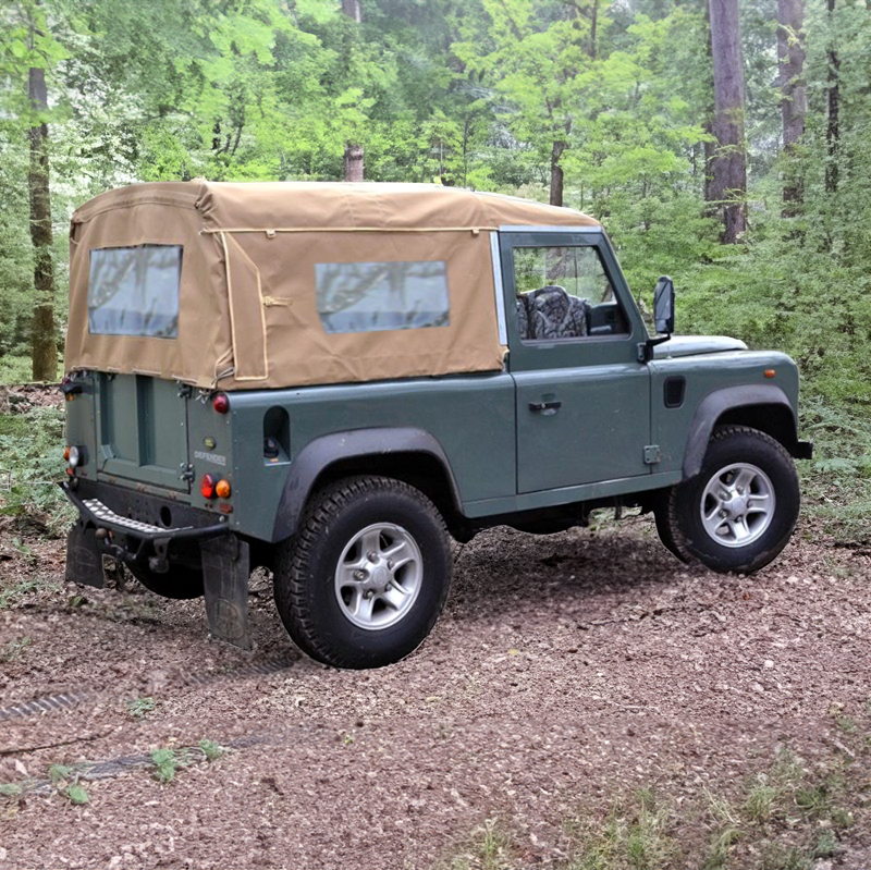 Land Rover Defender 90 Td5 Td4 mit Soft Top Verdeck in sand beige aus Canvas im Wald. Im Hintergrund sind Bäume zu sehen. Das Verdeck hat ein Heckfenster und Seitenfenster. 