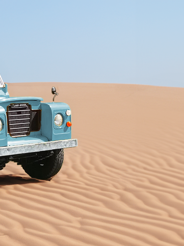 blauer restaurierter Land Rover Serie 3 auf einer Sand Düne mit blauem Himmel im Hintergrund